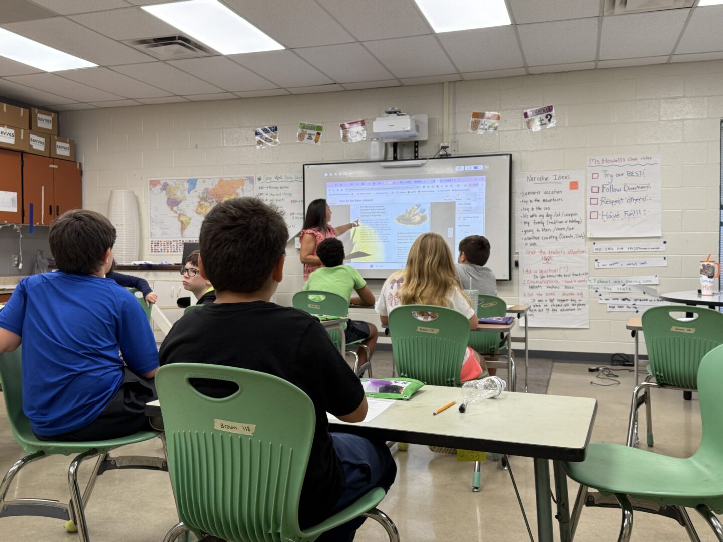Students attentively listen to a teacher presenting a lesson on a smartboard in a classroom.