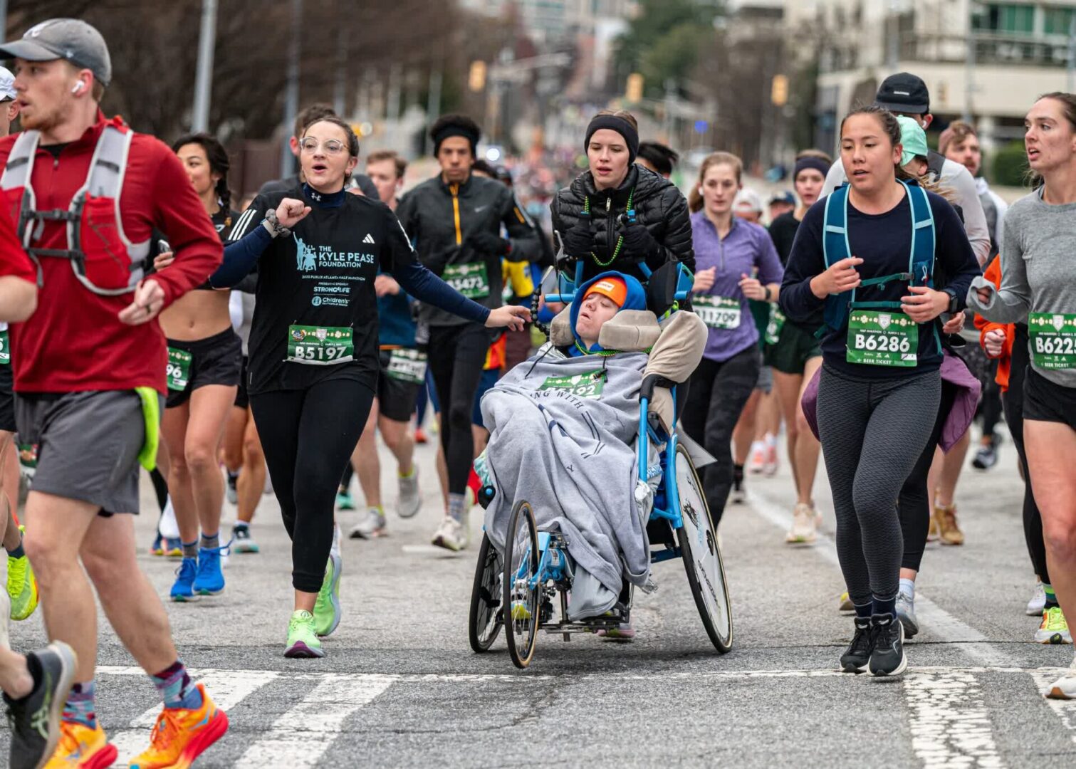 A group of marathon runners, including a participant in a wheelchair, race on a city street.