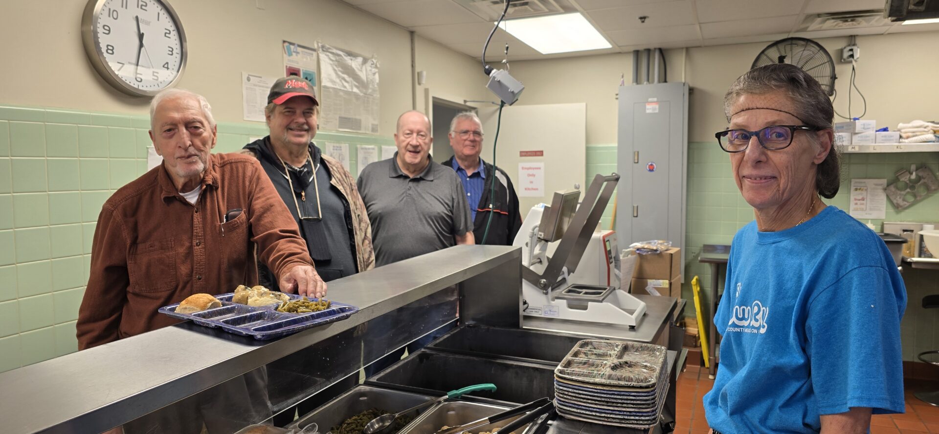 Three older men standing near a commercial fryer in a kitchen.