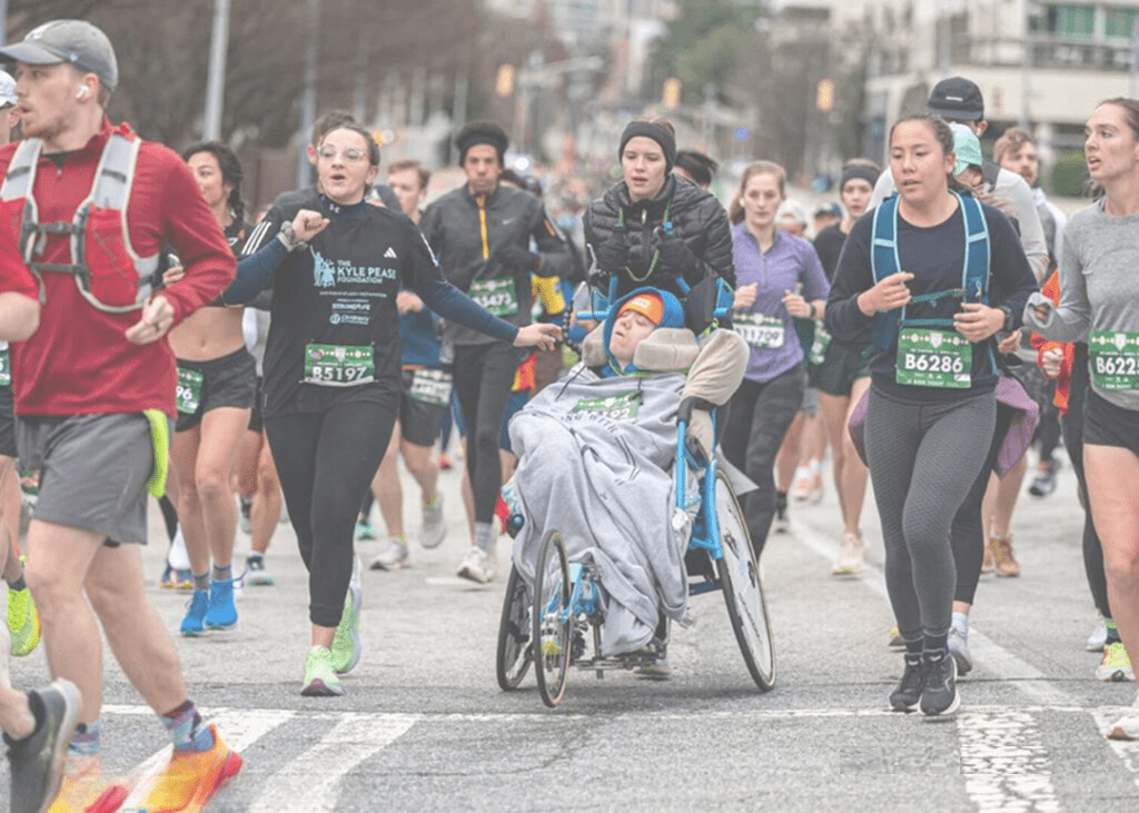 A diverse group of runners, including a participant in a wheelchair, race together outdoors.